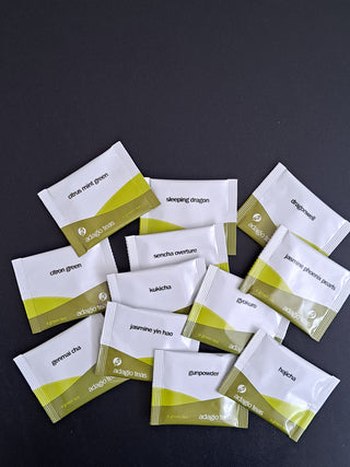 Multiple white and green packets green tea arranged on a dark surface
